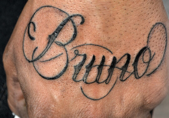 Tatouage lettrage sur la main du prénom "Bruno" style Chicano script.